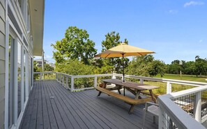 A wooden deck with a picnic table and umbrella, surrounded by a white railing and greenery.