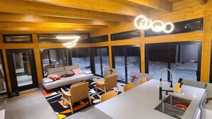 A modern interior with a sofa, chairs, a dining table, and a kitchen area. - The Retreat - Mountain chalet - piscine & spa (Sainte-Béatrix)