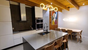 A modern kitchen with a central island, built-in appliances, and wooden ceiling beams. - The Retreat - Mountain chalet - piscine & spa (Sainte-Béatrix)