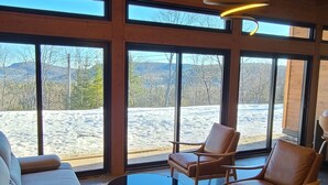 A spacious room with a wooden ceiling, large windows, a sofa, and leather chairs. - The Retreat - Mountain chalet - piscine & spa (Sainte-Béatrix)
