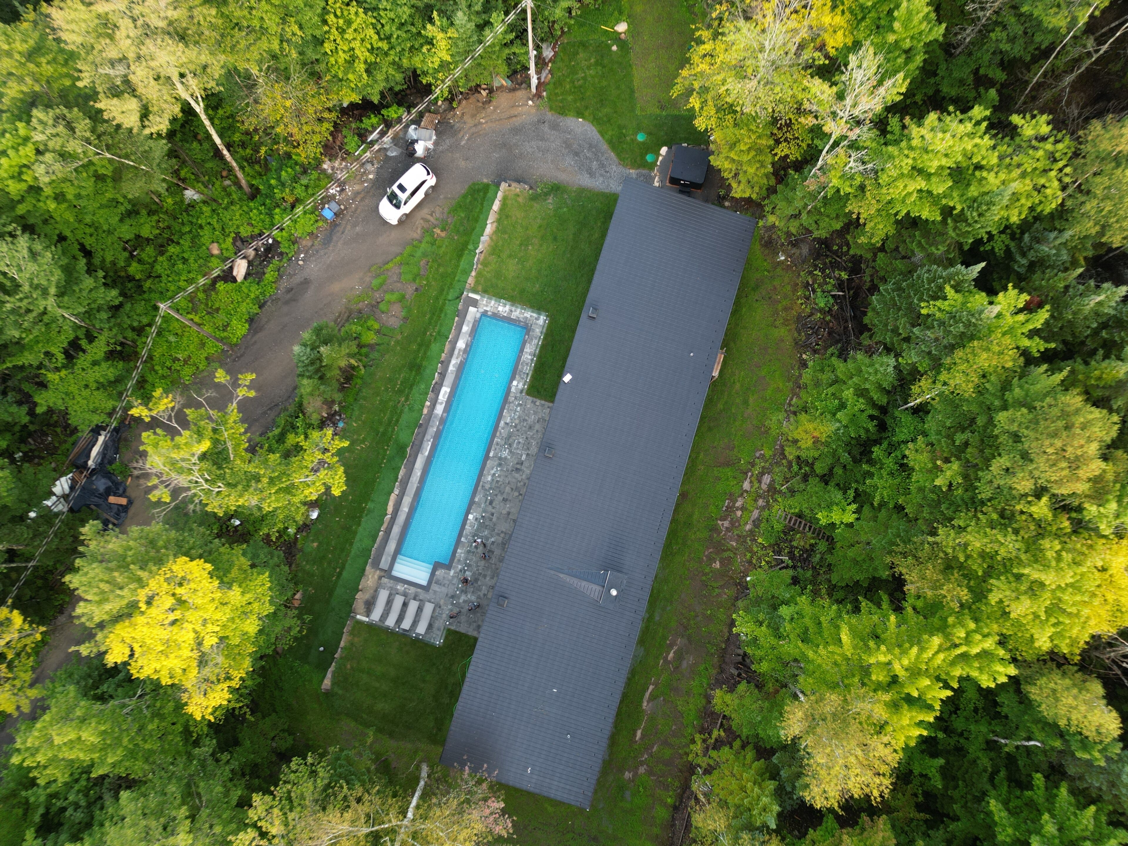 Vue aérienne d’une maison dotée d’une piscine rectangulaire, entourée d’arbres verdoyants.