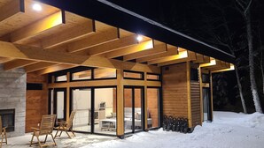 A modern wooden cabin with a stone fireplace, large sliding glass doors, and a cozy seating area. - The Retreat - Mountain chalet - piscine & spa (Sainte-Béatrix)