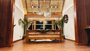 Una habitación con un banco de madera, un ventanal con cortinas y un techo de techo de paja.