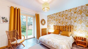Un dormitorio con una cama grande, una silla de mimbre, una mesita de noche de madera y una ventana con cortinas.