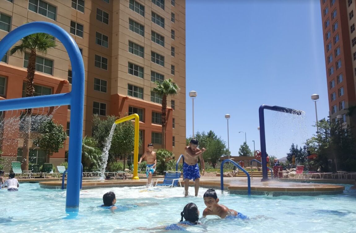 A swimming pool area with water features and a tall building in the background.