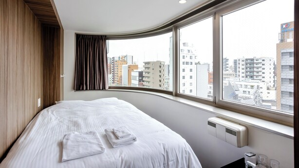 Una habitación de hotel con una cama grande, vistas de la ciudad a través de un ventanal amplio y un aire acondicionado integrado.
