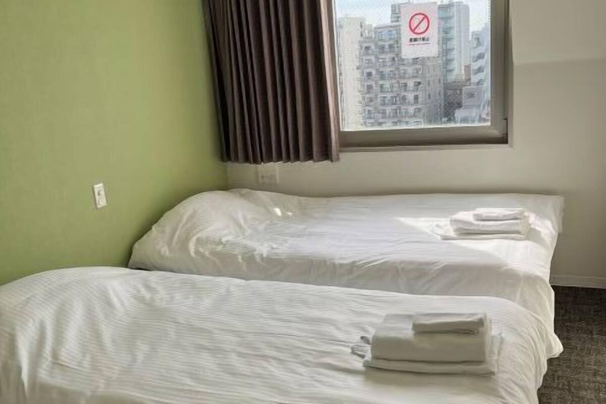 Una habitación de hotel con dos camas, una ventana con vista a edificios y una cortina.