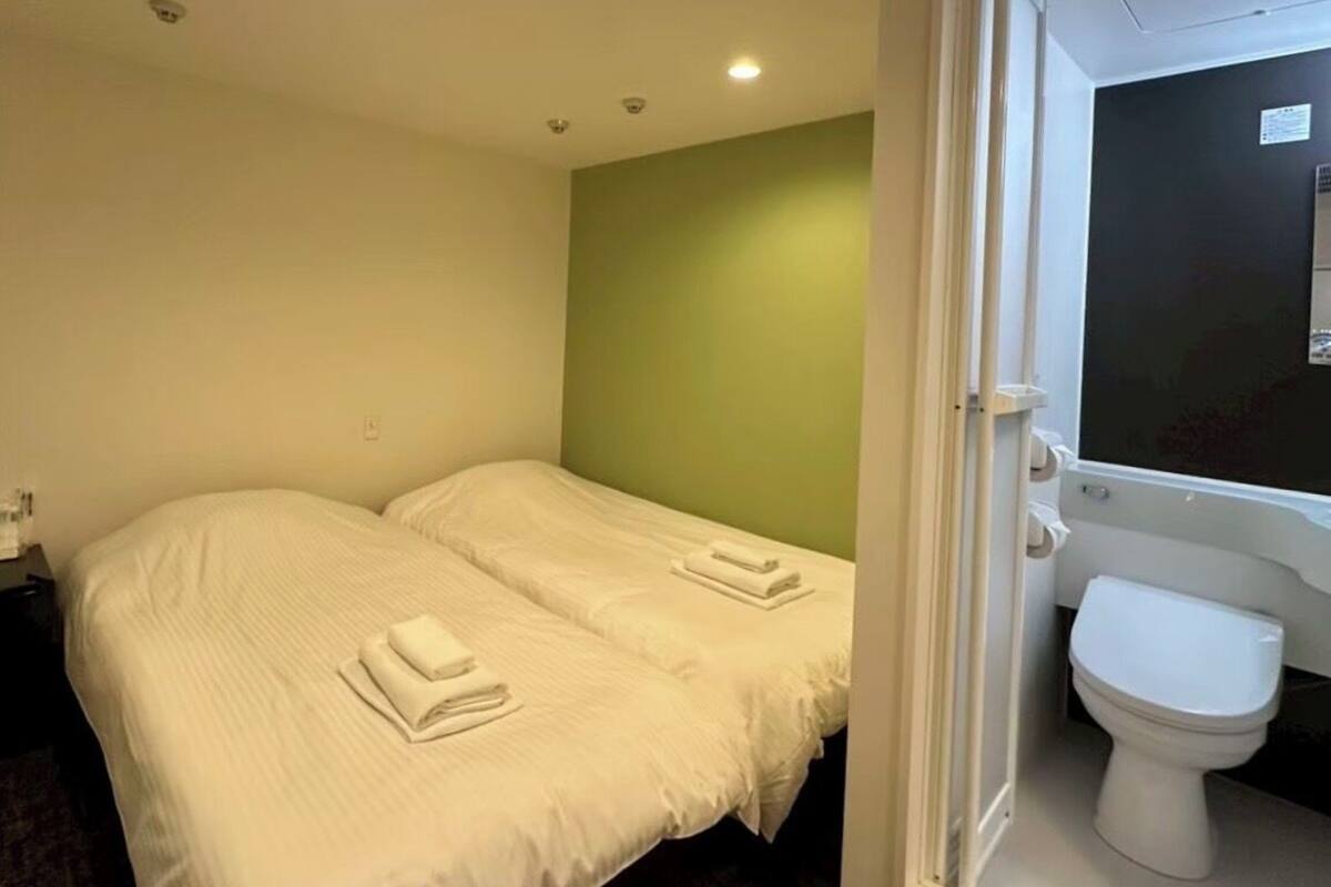 Una habitación de hotel con dos camas, una pared de acento verde, un inodoro blanco y una ventana.