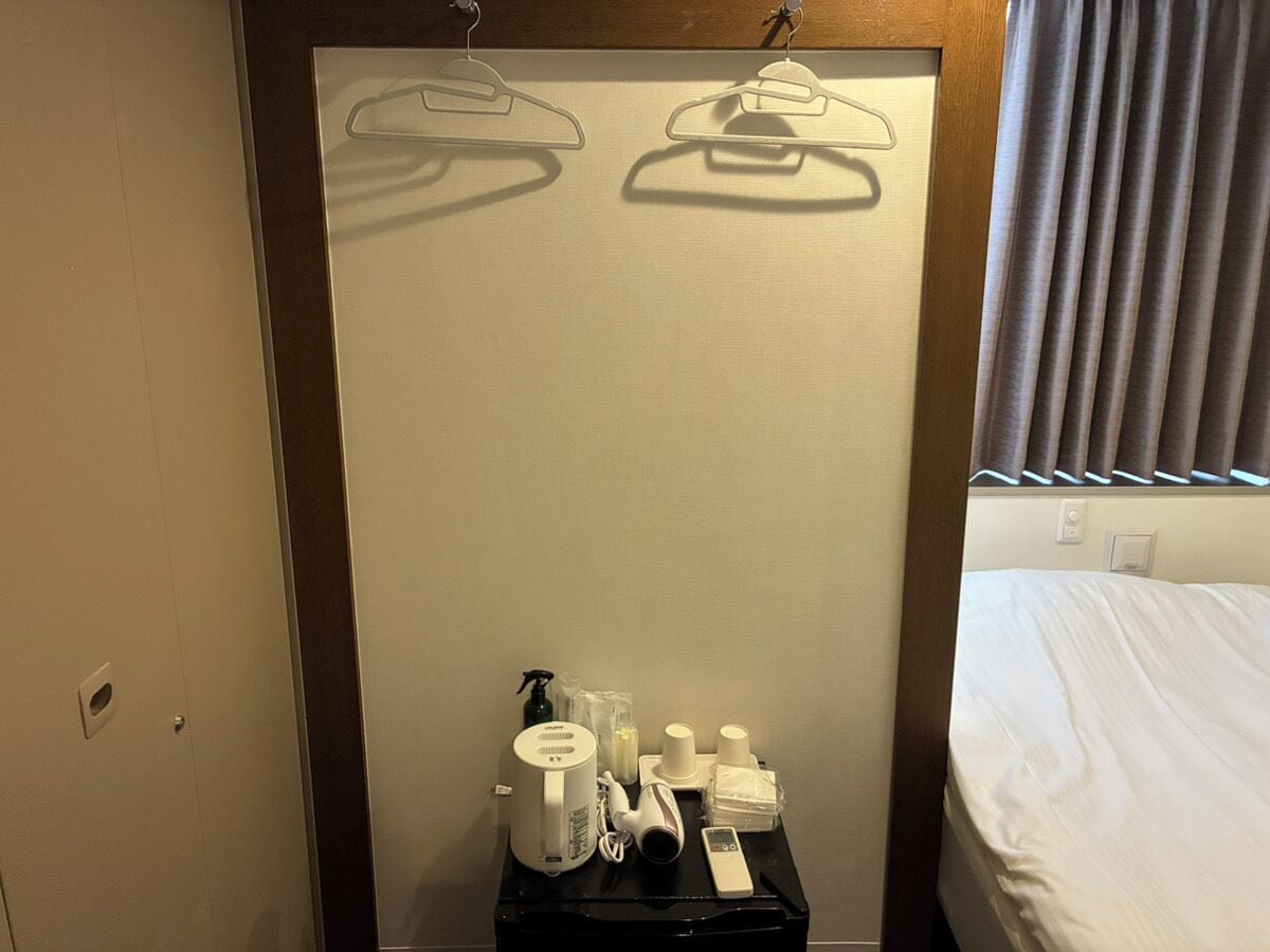 A hotel room with a bed, a small table with toiletries, and a wall-mounted towel rack.