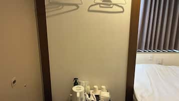 Een hotelkamer met een bed, een klein tafeltje met toiletartikelen en een wandrek voor handdoeken.