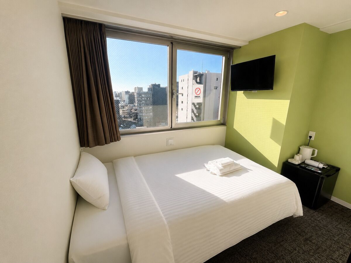Une chambre d’hôtel avec un lit, un téléviseur fixé au mur et une fenêtre avec des rideaux.