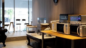 Una cocina con microondas, horno y cafetera sobre una encimera. Se ven sillas y una mesa al fondo.