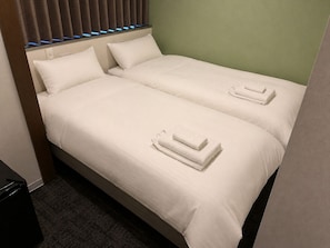 Habitación de hotel con dos camas, cada una con ropa blanca y toallas dobladas.