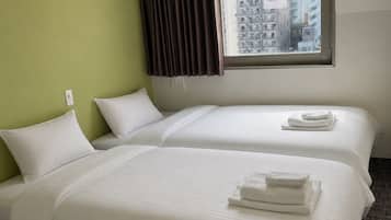 A hotel room with two beds, a window with a view of buildings, and a no-smoking sign.