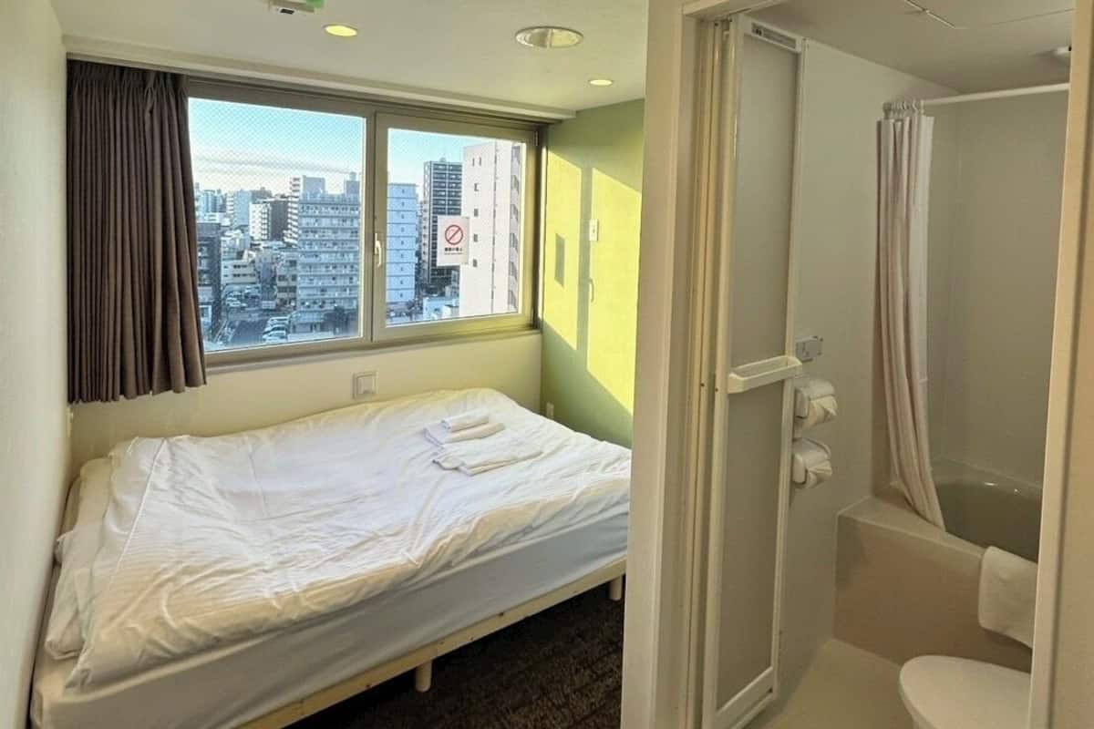 Una cama individual con vistas a la ciudad, una ducha y un inodoro en una habitación pequeña.