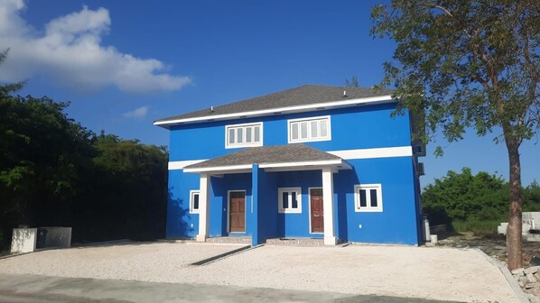 A two-story house with a blue exterior and white trim, a front porch, and a gravel driveway. - Cozy 2-bedroom townhome in lovely gated community in Nassau with WiFi and AC. (Nassau)