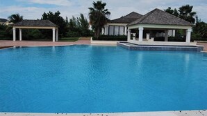 Una piscina con dos gazebos, rodeada de palmeras y un cielo despejado.