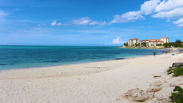 Una playa con cielo azul despejado, orilla arenosa y un edificio de varios pisos al fondo.