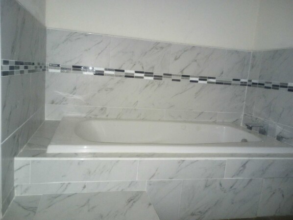 Un baño con pared de azulejos de mármol y una bañera.