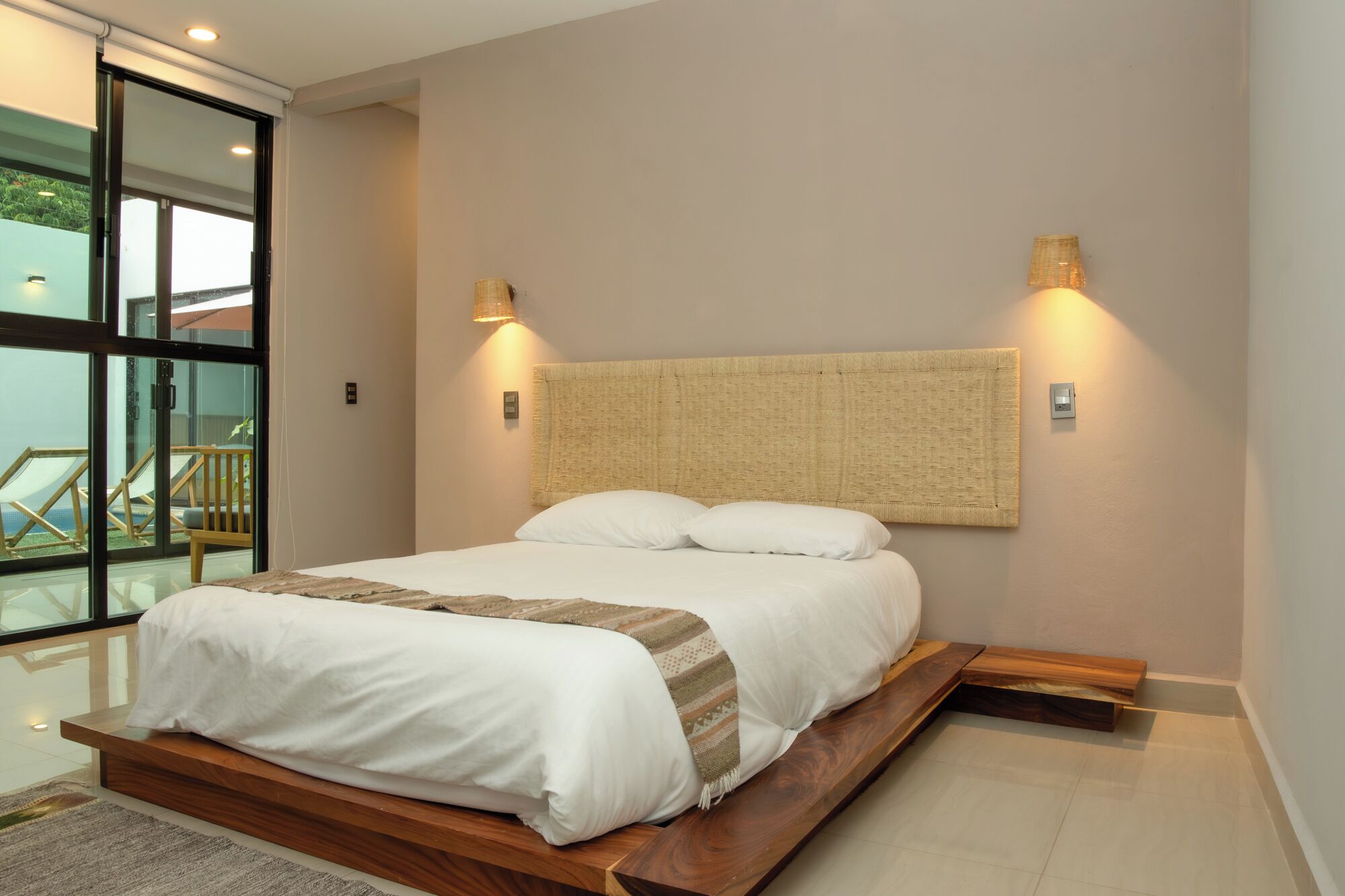 A modern bedroom with a large bed, a wooden bench, and a view of a balcony.