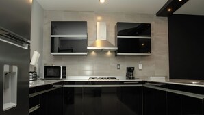 A modern kitchen with black cabinets, a stainless steel range hood, a microwave, and a gas stove. - Casa Mosso  (Oaxaca)
