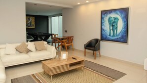 A modern living room with a white sofa, a wooden coffee table, a black armchair, a pool table, and a large painting of an elephant. - Casa Mosso  (Oaxaca)