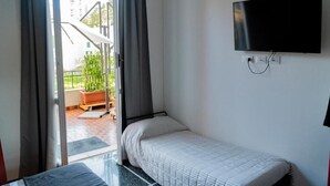 A small, single-bed room with a TV mounted on the wall, a sliding glass door leading to an outdoor area with a staircase and potted plants. - Tuibeds (Arenzano)