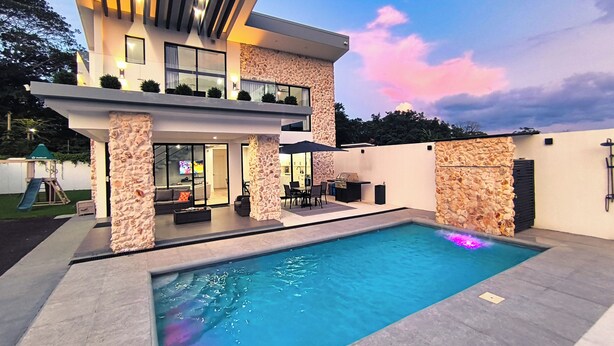 A modern two-story house with a swimming pool, stone pillars, and outdoor seating area. - Arenal Harmony Villa - Private heated pool! (La Fortuna)