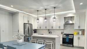 A modern kitchen with white cabinets, a stainless steel refrigerator, a black stove, and a blue dining table with chairs. - Arenal Harmony Villa - Private heated pool! (La Fortuna)