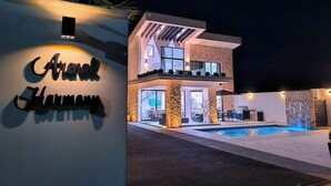Ein modernes, zweistöckiges Gebäude mit Pool, Steinsäulen und einem Schild mit der Aufschrift 'Arenal Harmony'.