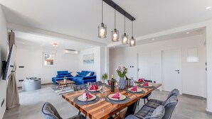 A modern dining area with a wooden table set for six, grey upholstered chairs, and a blue sofa in the background.