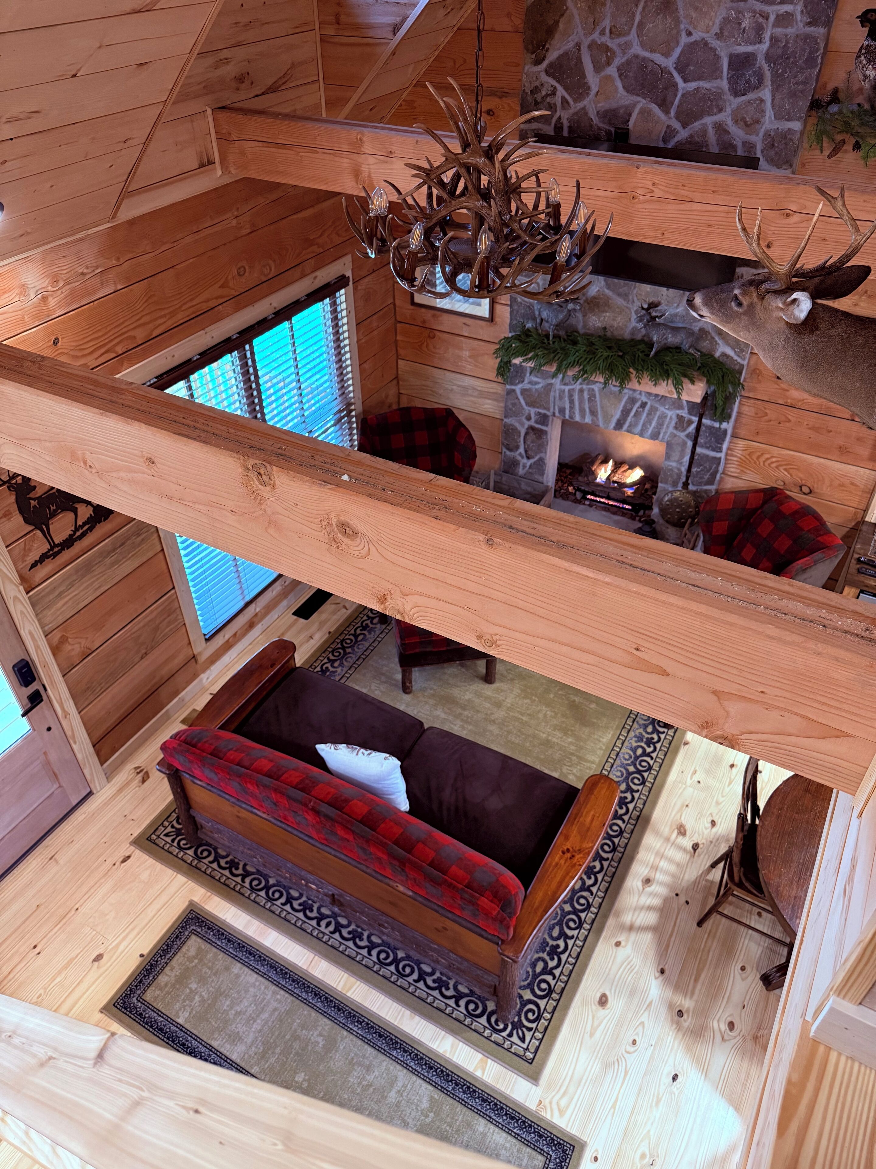 A cozy cabin interior with a stone fireplace, a red and black plaid sofa, and a wooden ceiling.