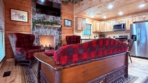 A cozy cabin interior with a stone fireplace, wooden furniture, and a kitchen area.