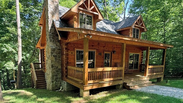 A log cabin with a stone chimney, wooden porch, and multiple windows.
