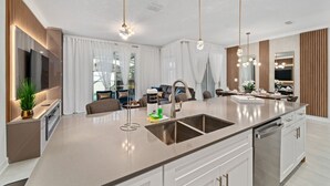A modern kitchen with a large island, stainless steel appliances, and pendant lighting.