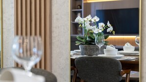 A dining area with a table set for two, featuring a potted orchid, a glass, and white dishes.