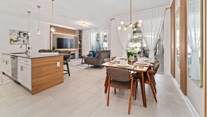 A modern kitchen with a central island, a dining area with a wooden table and chairs, and a living room with a sofa and TV.