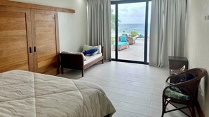 A hotel room with a bed, a sofa, a chair, and a view of the ocean. - Modern Oceanfront  4-bedroom house with pool, WiFi, AC in lovely town of Cabrera (Dominican Republic)