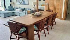 A dining area with a wooden table and wicker chairs, a sofa with cushions, and a painting on the wall. - Modern Oceanfront  4-bedroom house with pool, WiFi, AC in lovely town of Cabrera (Dominican Republic)