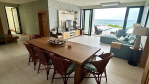 A spacious living area with a wooden dining table, wicker chairs, a sofa, and a view of the ocean. - Modern Oceanfront  4-bedroom house with pool, WiFi, AC in lovely town of Cabrera (Dominican Republic)
