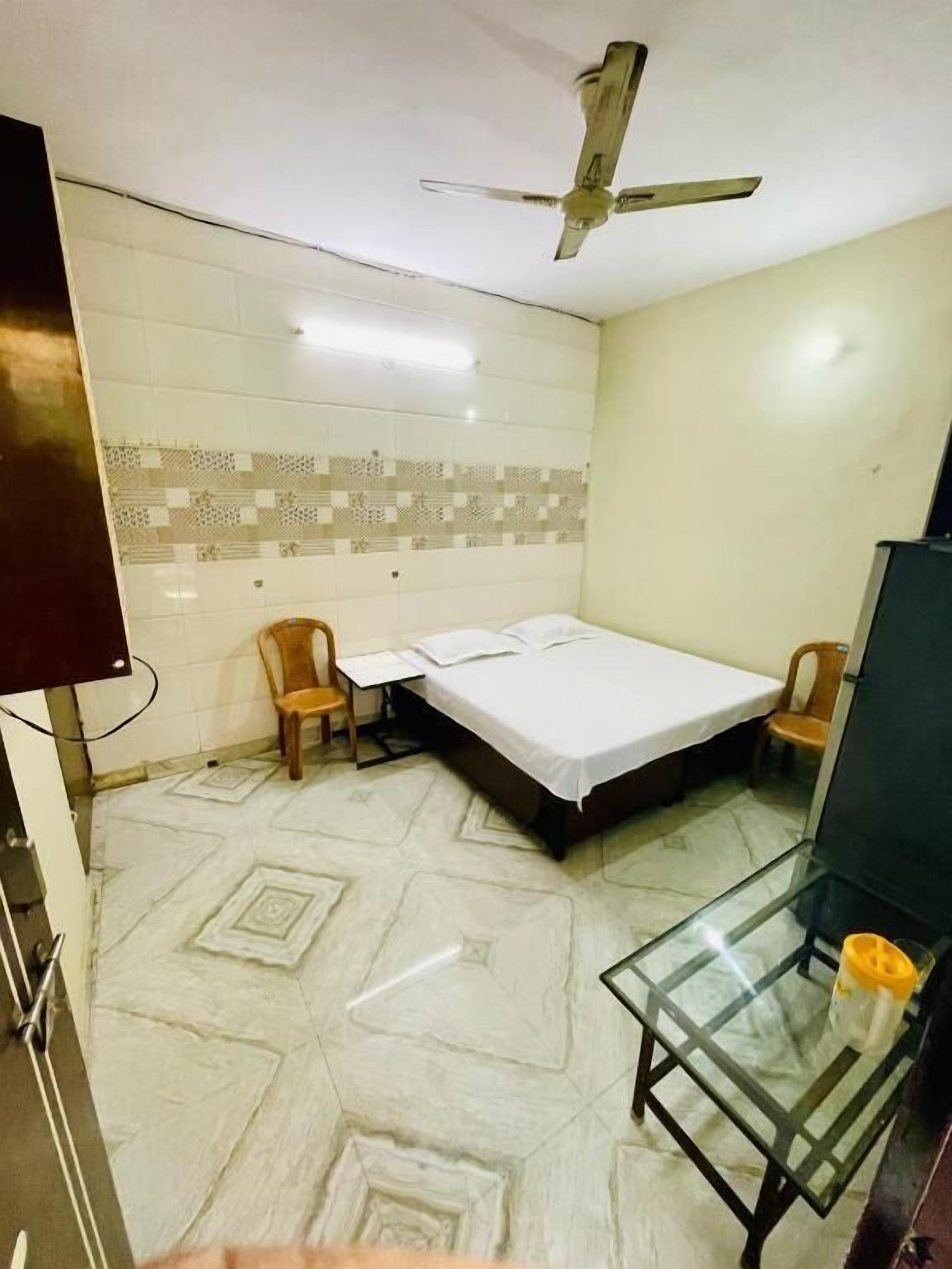 A small, clean room with a bed, a desk, a chair, a television, and a ceiling fan.