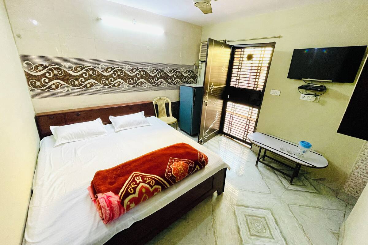 A hotel room with a bed, a desk, a television, and a window with blinds.