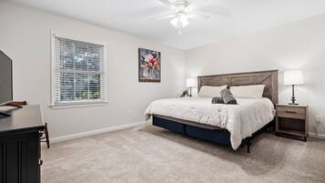 A bedroom with a bed, bedside tables, a ceiling fan, a window with blinds, and a painting on the wall.