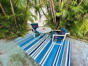 Relax in a serene outdoor space surrounded by lush greenery and tropical plants, with a round table and two comfortable chairs.