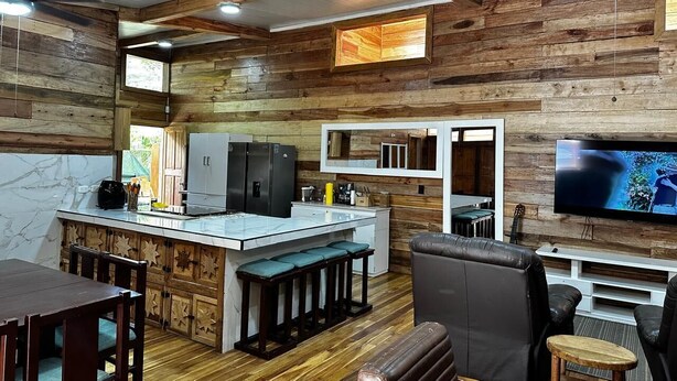 A rustic kitchen with wooden walls, a marble countertop, and a dining area with a wooden table and chairs.