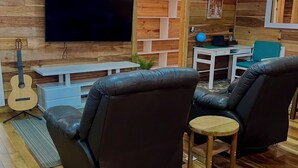 A cozy living room with wooden walls, a flat-screen TV, a guitar, and leather armchairs.