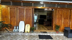 A wooden-floored lobby with surfboards and a surfboard stand, potted plants, and a black mat at the entrance.
