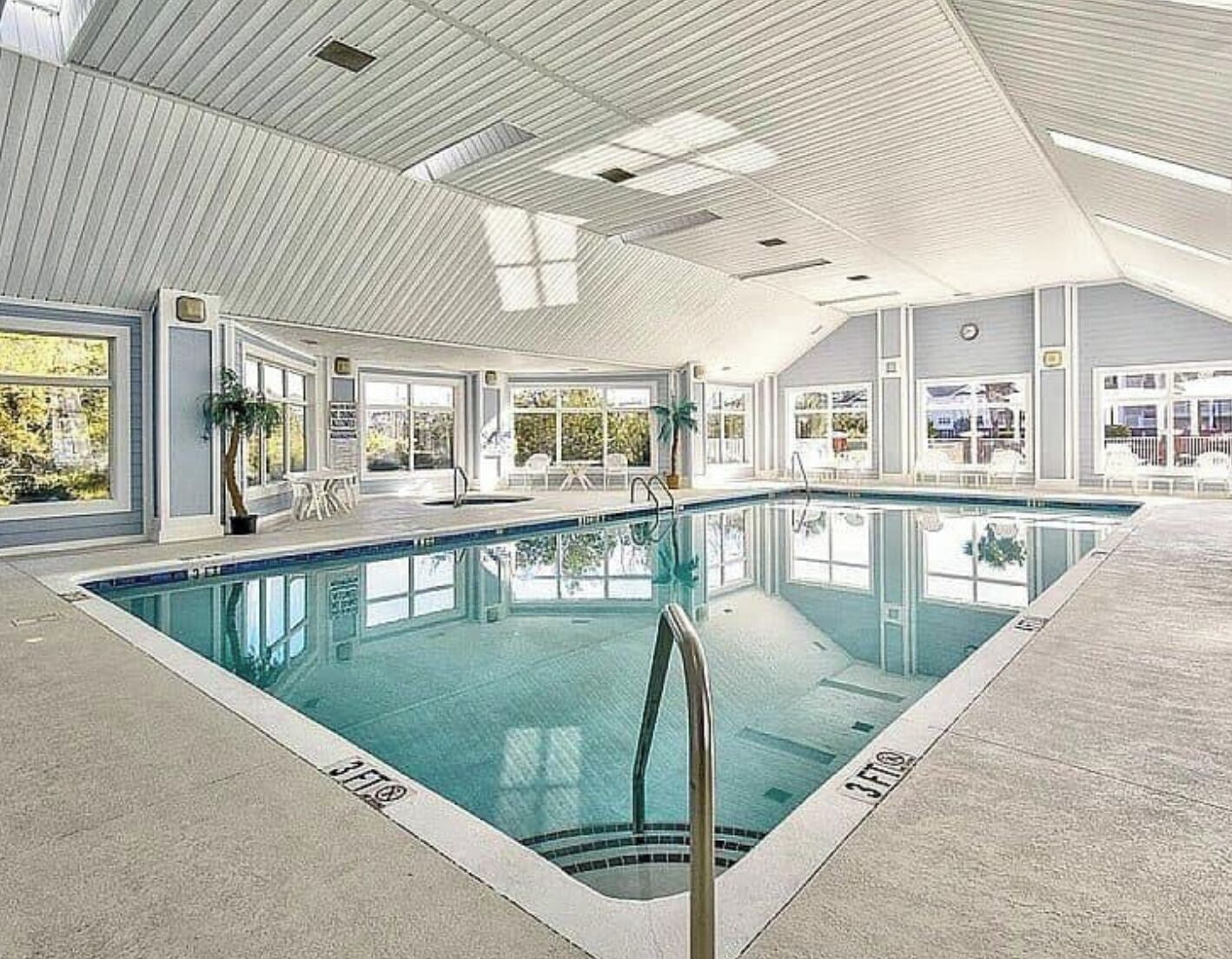 Ein Hallenbad mit klarem Wasser, umgeben von Fenstern und Topfpflanzen.