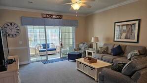 A living room with a large clock, a ceiling fan, and a sign reading "BEACH HOUSE". - Charming 3-bedroom Golf Villa in Murrells Inlet South Carolina (Murrells Inlet)
