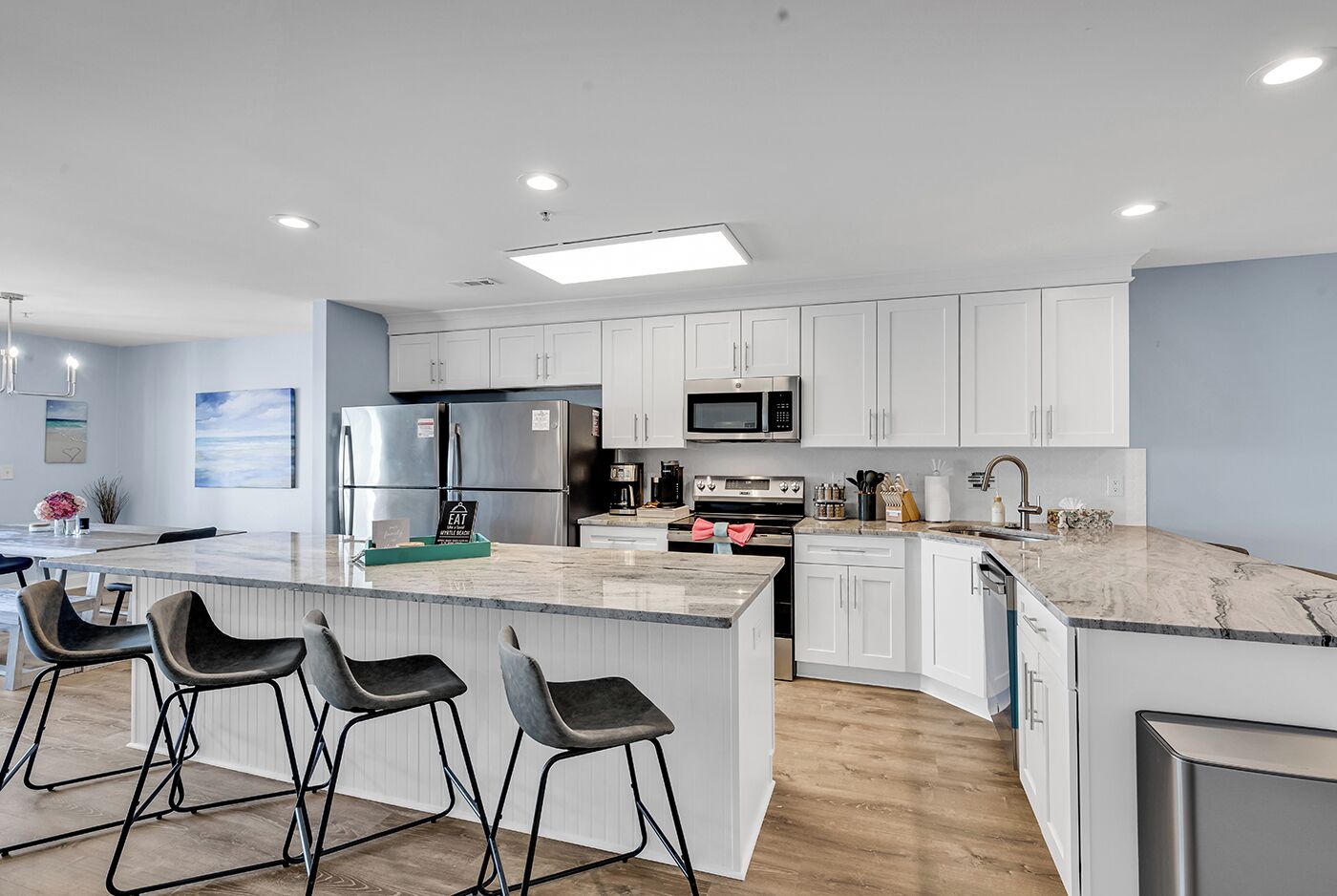 A modern kitchen with white cabinets, stainless steel appliances, a marble countertop, and bar stools.